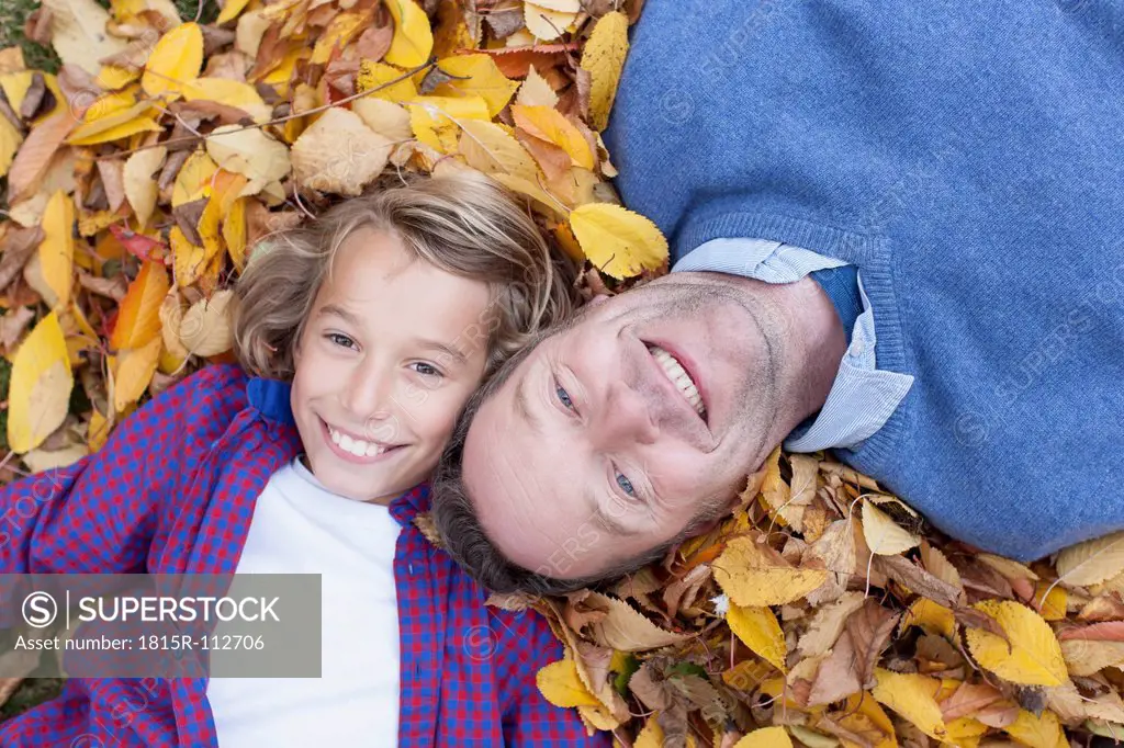 Germany, Leipzig, Father and son lying on leaves, smiling