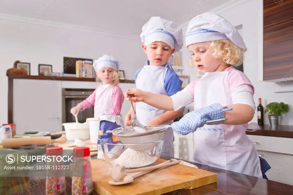Germany, Girls and boy sifting flour in bowl