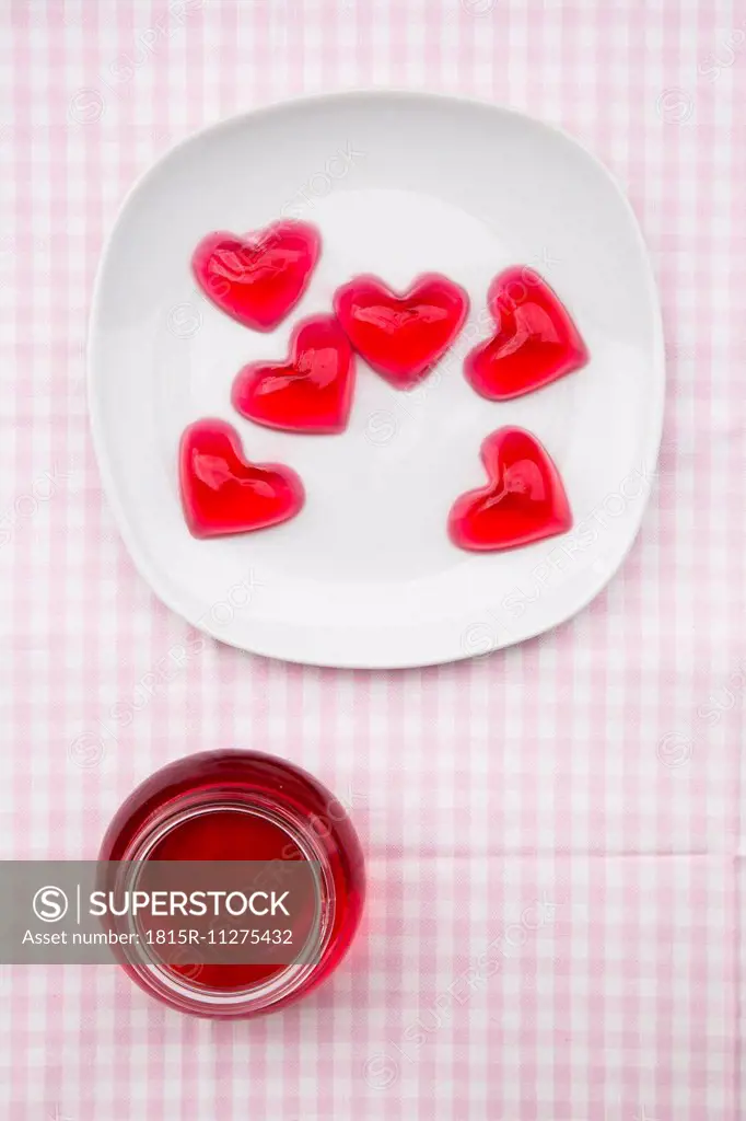 Plate of red hearts shaped of cherry jelly and preserving jar of cherry jelly on checkered cloth