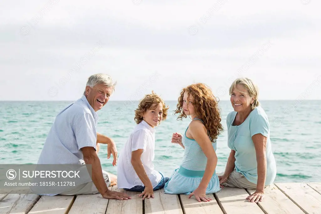 Spain, Grandparents with grandchildren sitting on jetty, smiling, portrait