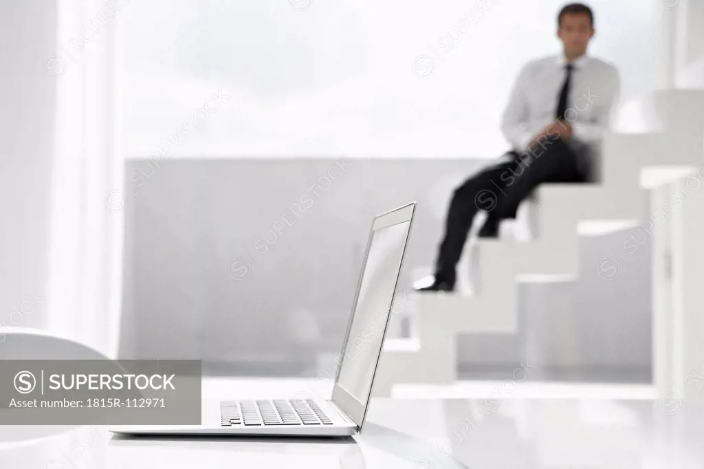 Spain, Businessman sitting on stairs, laptop in foreground