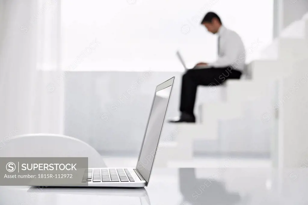 Spain, Businessman using laptop on stairs, laptop in foreground