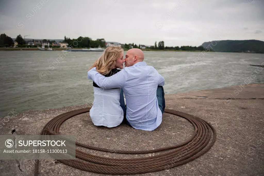 Germany, Rhineland-Palatinate, young couple kissing at waterside of Rhine river