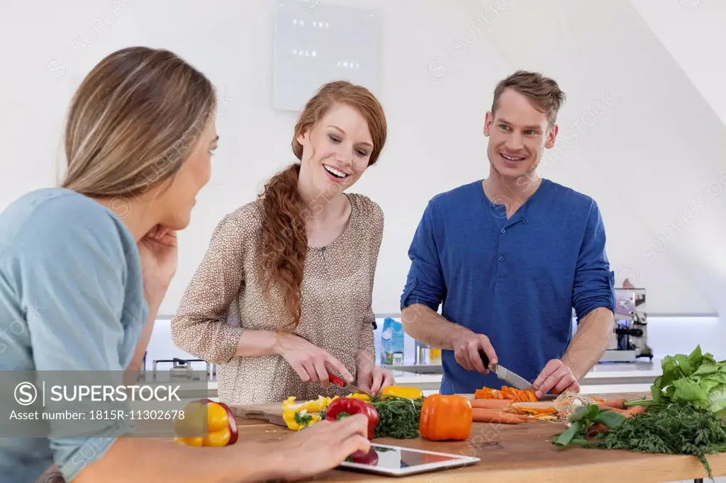 Three friends preparing meal and using tablet computer