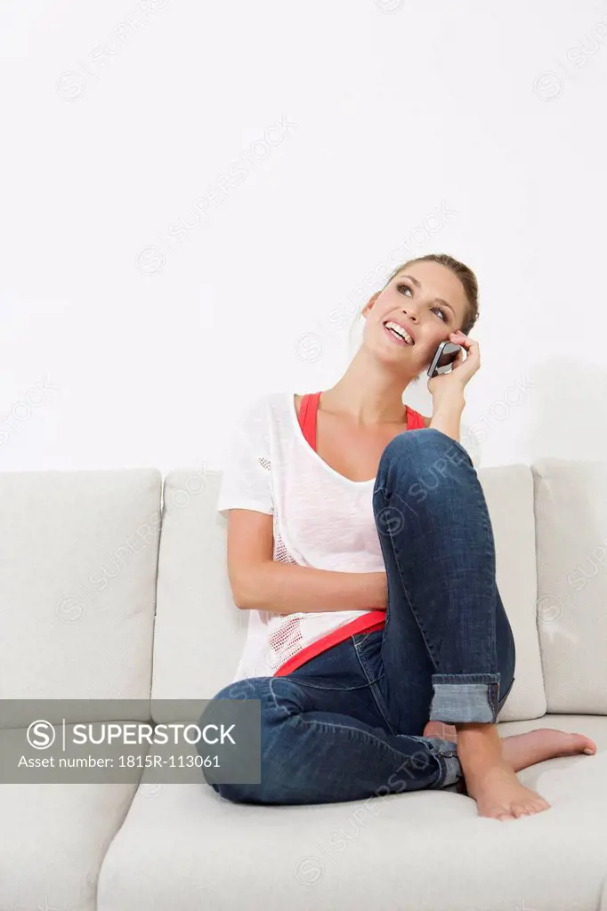 Germany, Berlin, Young woman sitting on couch and using smart phone