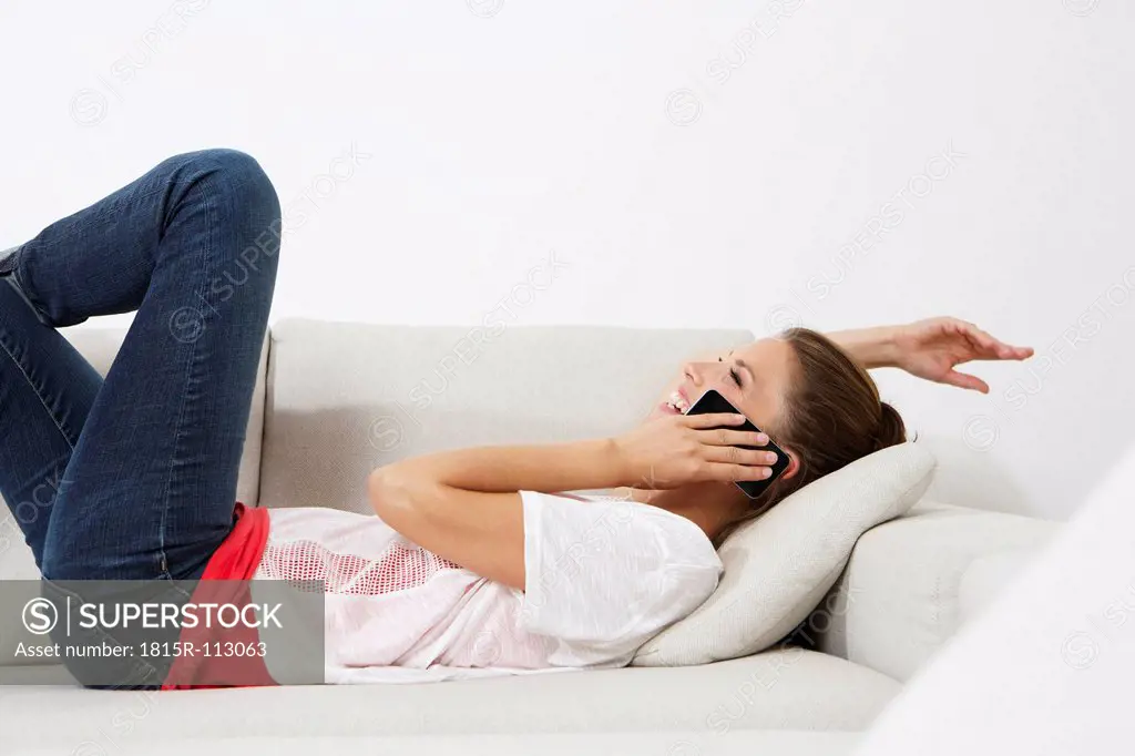 Germany, Berlin, Young woman lying on couch and using smart phone