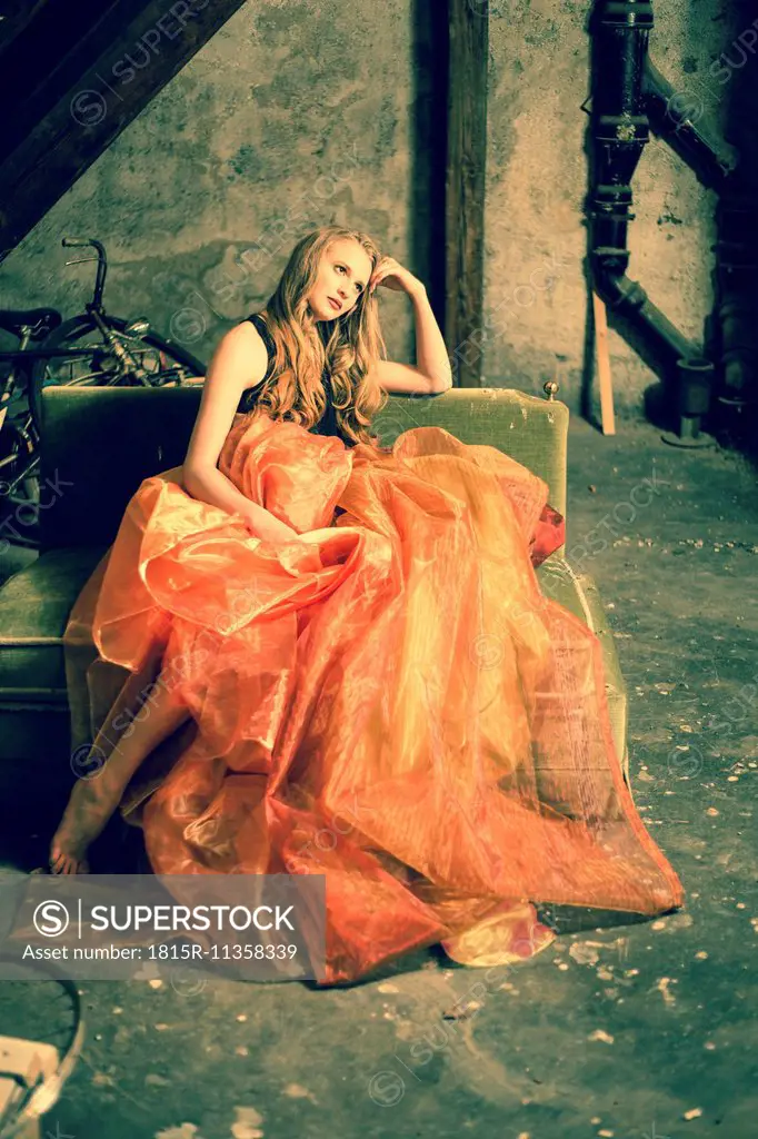 Portrait of young woman sitting at attic wearing orange skirt