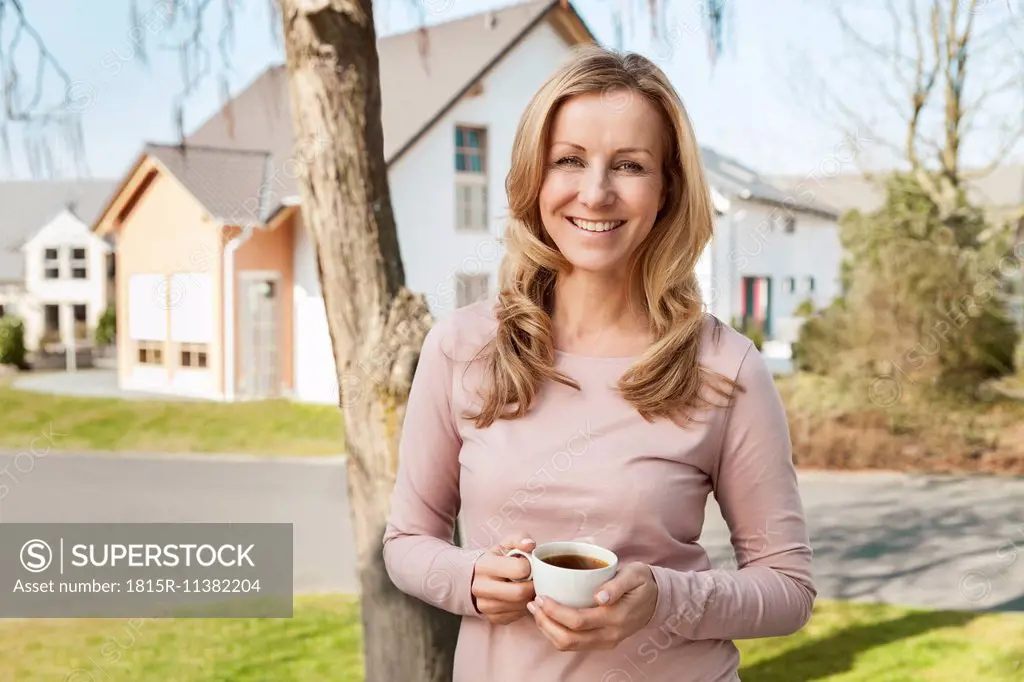 Smiling woman with cup of coffee standing in front of residential area