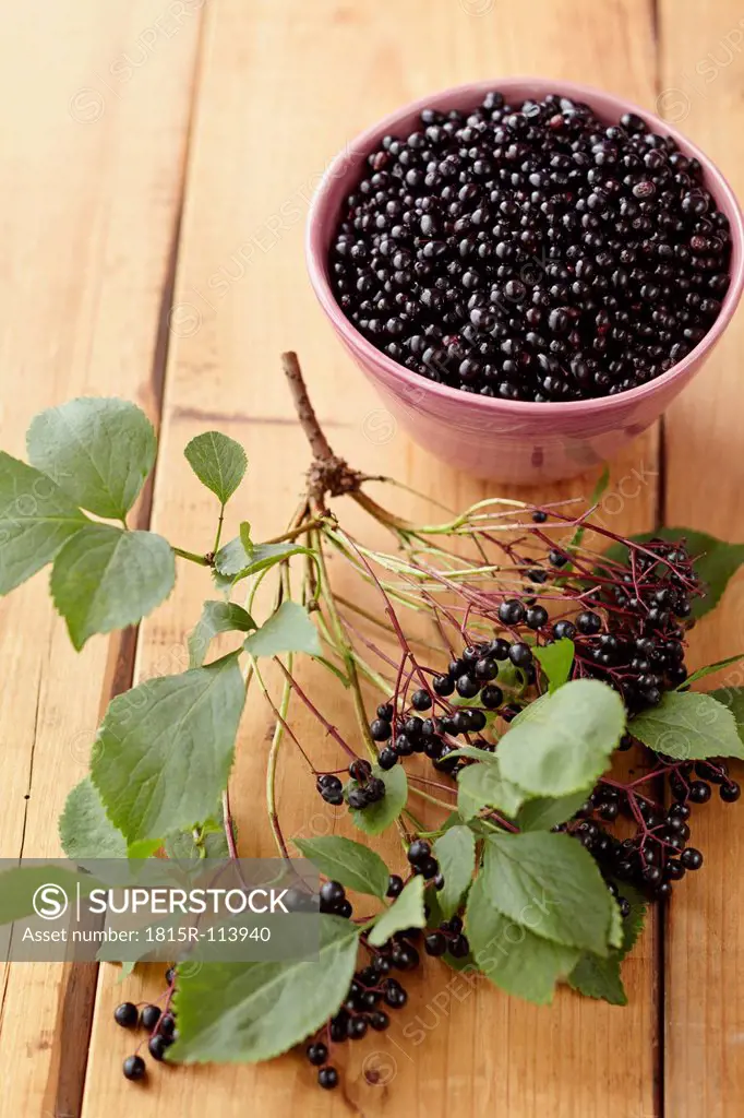 Bowl full of elderberries with branch on wooden table