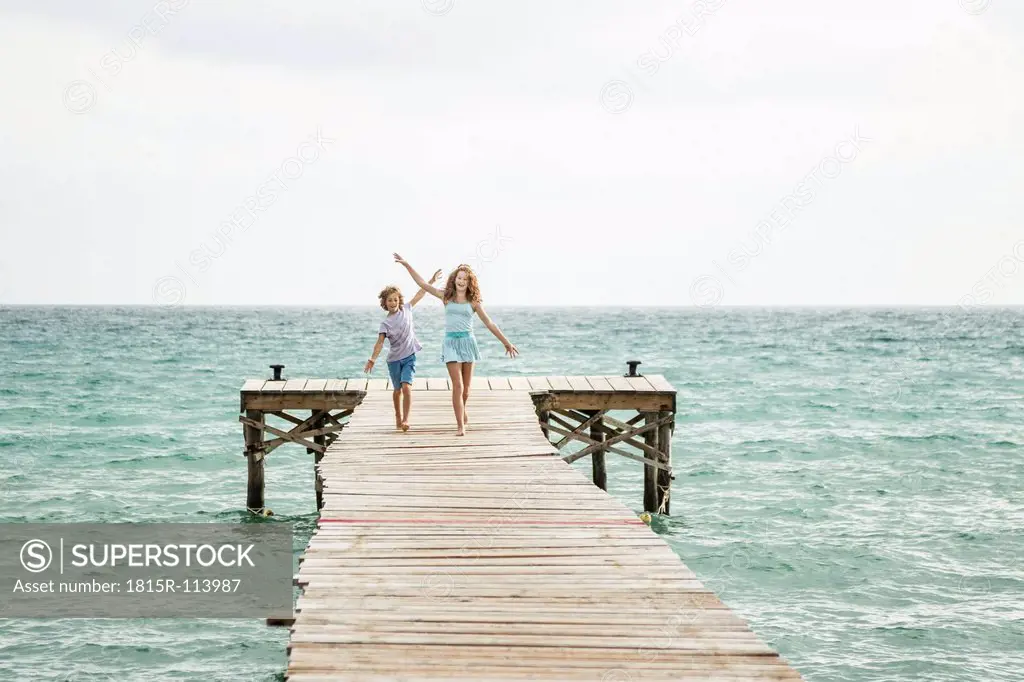 Spain, Girl and boy running on jetty at the sea