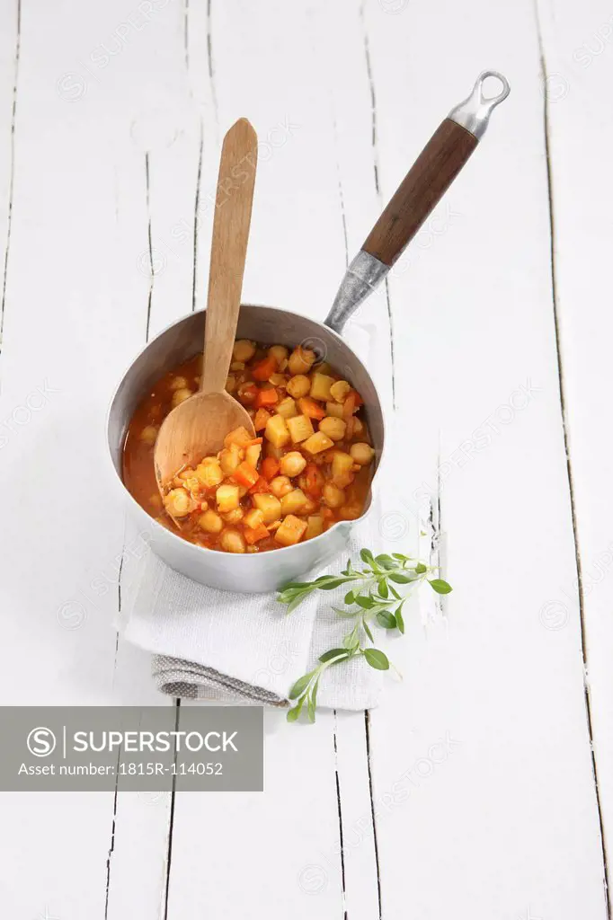 Potato chickpea soup in pot with wooden spoon on table