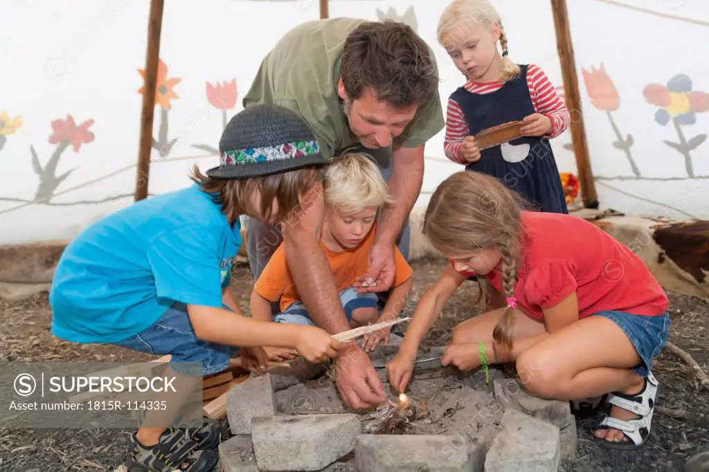 Germany, Munich, Father with children preparing camp fire in tent