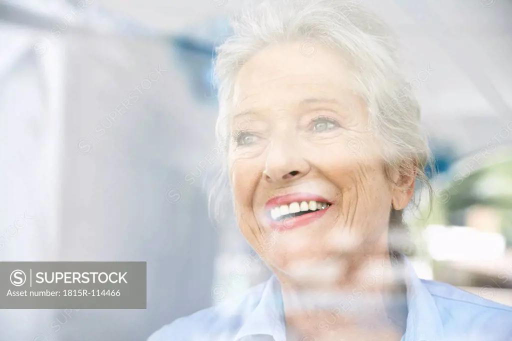 Spain, Senior woman looking through window, smiling