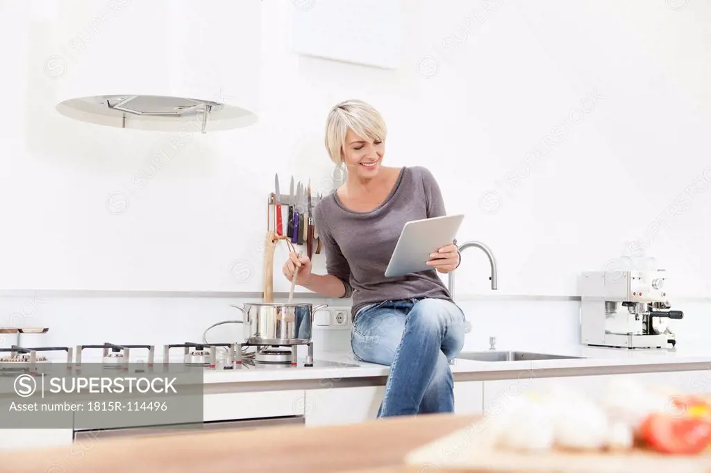 Germany, Bavaria, Munich, Woman watching digital tablet and preparing food