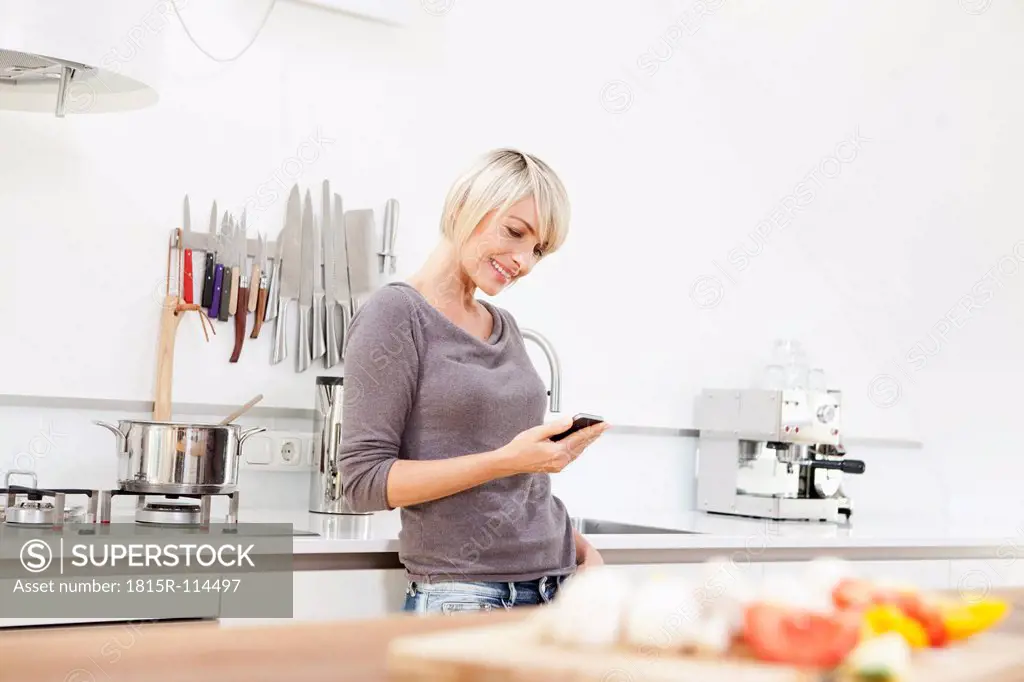 Germany, Bavaria, Munich, Woman using mobile in kitchen