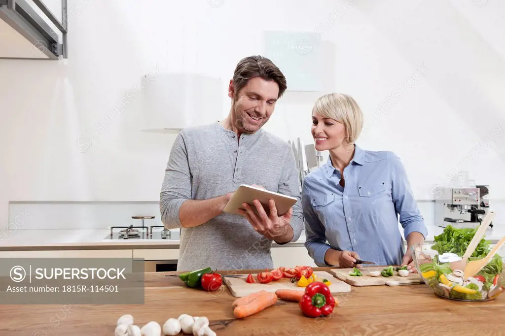 Germany, Bavaria, Munich, Mature couple preparing food while looking digital tablet