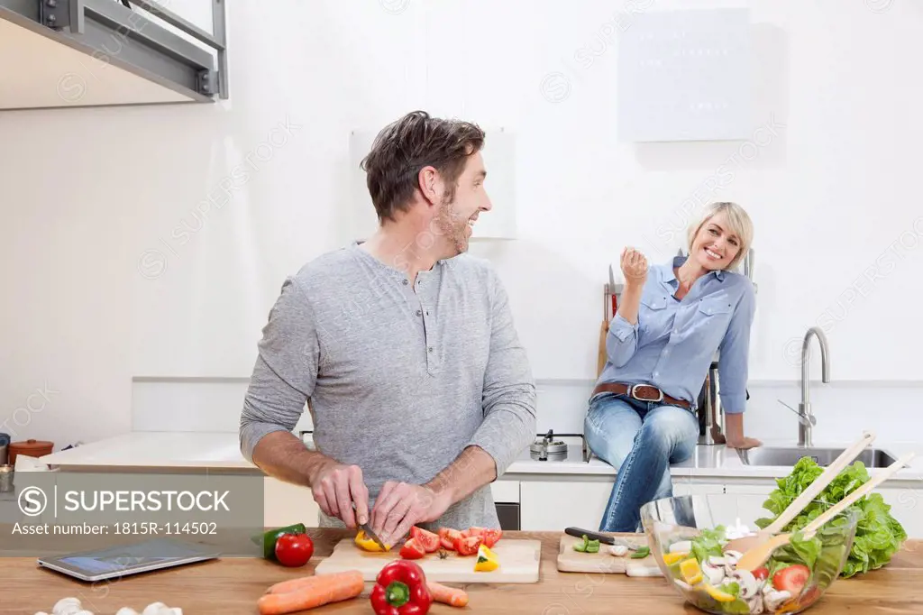 Germany, Bavaria, Munich, Mature man chopping vegetables, woman sitting in background