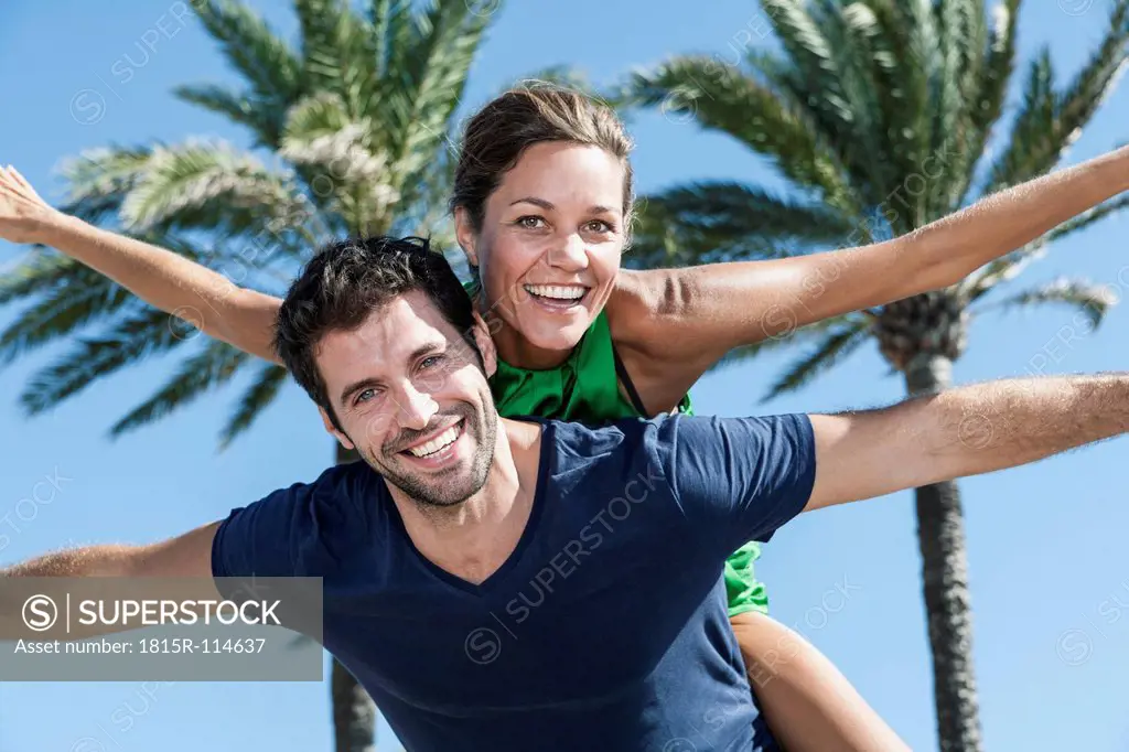 Spain, Mid adult man giving piggy back ride to woman, smiling