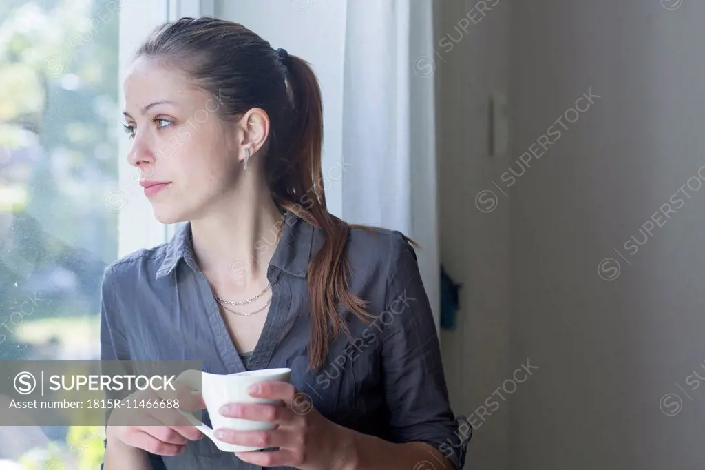 Young woman with cup of coffee looking through window