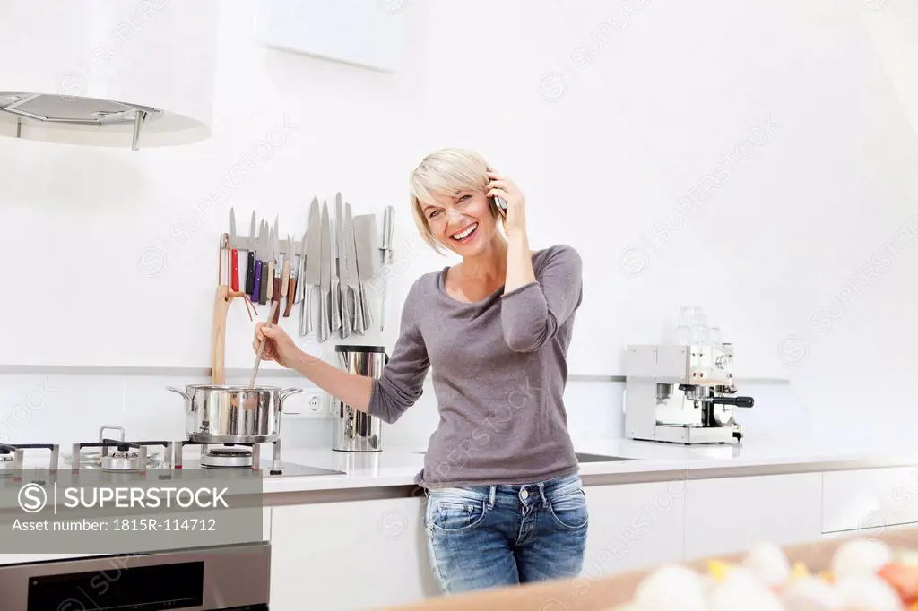 Germany, Bavaria, Munich, Woman using mobile in kitchen and preparing food