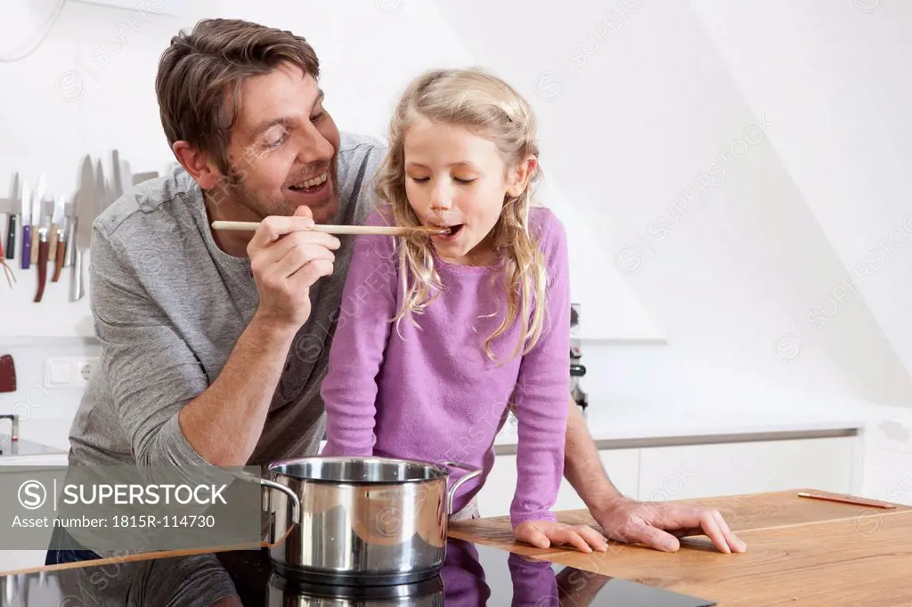 Germany, Bavaria, Munich, Father feeding daughter in kitchen, smiling