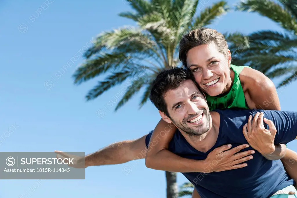 Spain, Mid adult man giving piggy back ride to woman, smiling