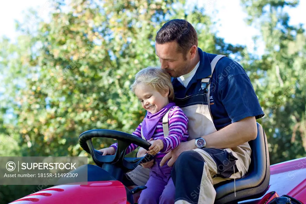 Father and little daughter driving together on lawn mower