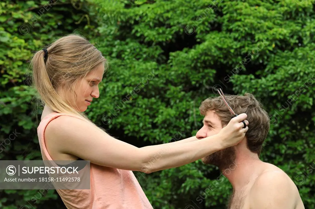 Young woman cutting hair of her boyfriend in the garden