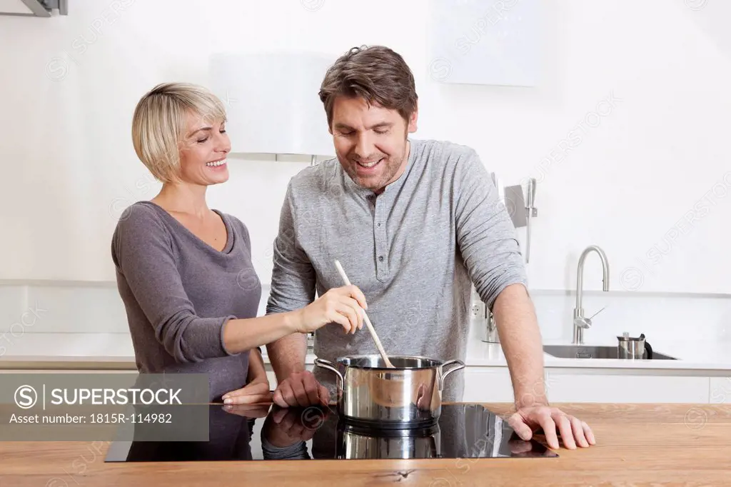 Germany, Bavaria, Munich, Mature couple cooking food in kitchen, smiling