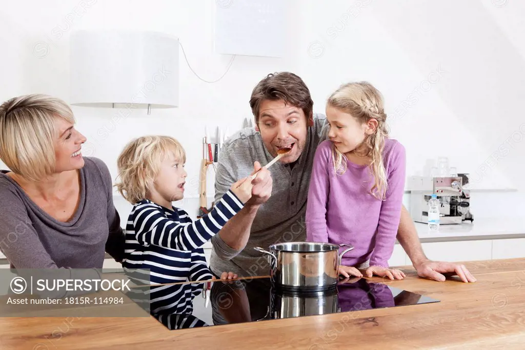 Germany, Bavaria, Munich, Family preparing food in kitchen while boy feeding father