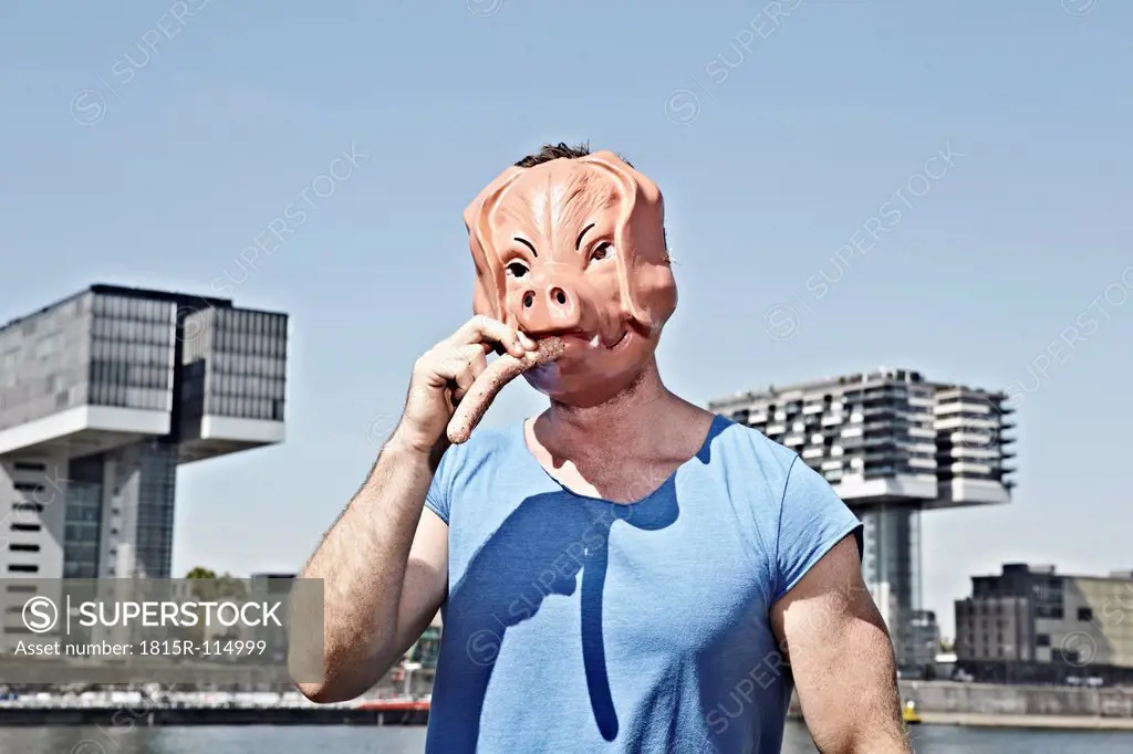 Germany, Cologne, Young man with pig mask eating sausage
