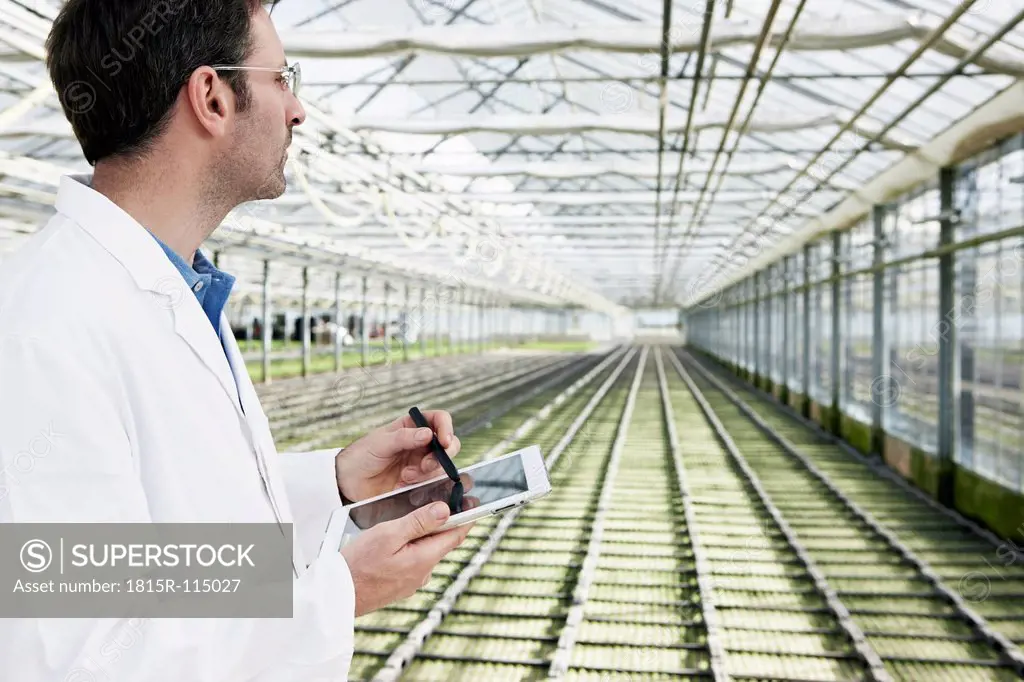 Germany, Bavaria, Munich, Scientist in greenhouse with digital tablet examining bed with seedlings