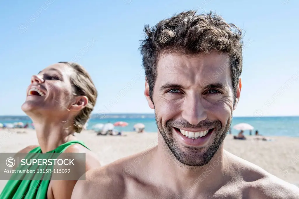 Spain, Mid adult couple sitting at beach, smiling