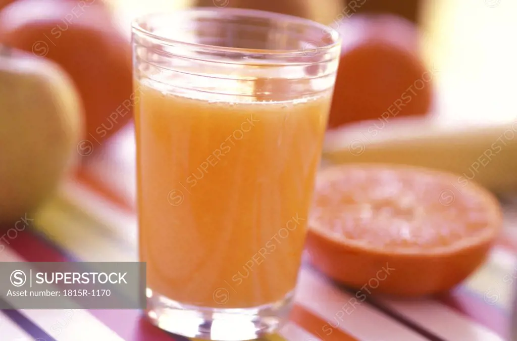 Glass of fresh orange juice, fruits in backround
