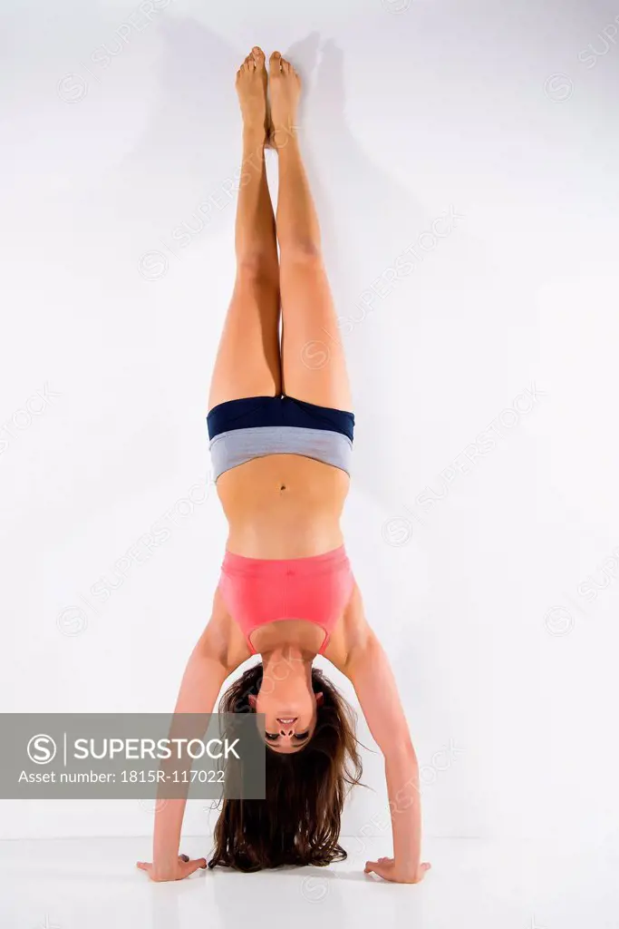 Young woman doing handstand against white background