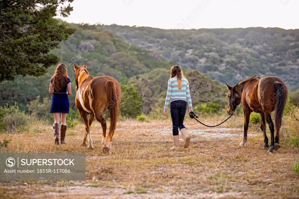 USA, Texas, Sisters walking with Quarterhorses near mountain
