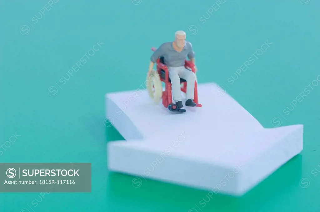 Figurine in wheelchair with arrow sign on green background