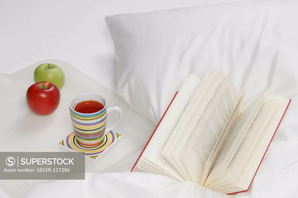 Germany, Rose hip tea with apples and book on bed