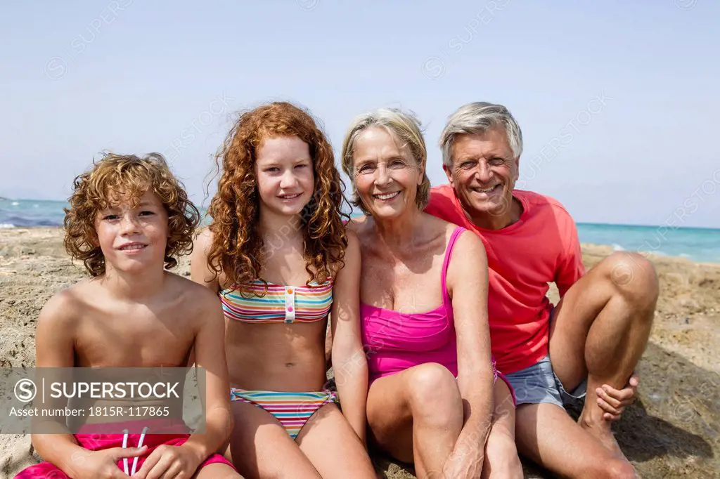 Spain, Grandparents with grandchildren sitting at beach, smiling, portrait