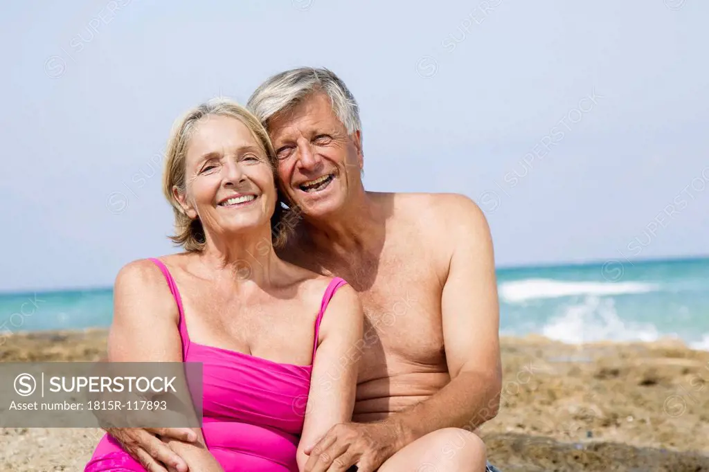 Spain, Senior couple sitting on rock at beach, smiling