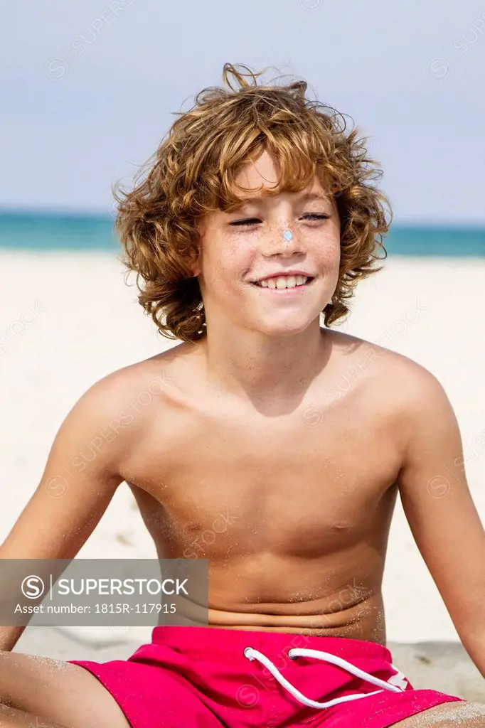 Spain, Boy sitting on beach, smiling