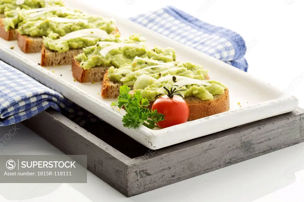 Bread slices with avocado spread on tray, close up