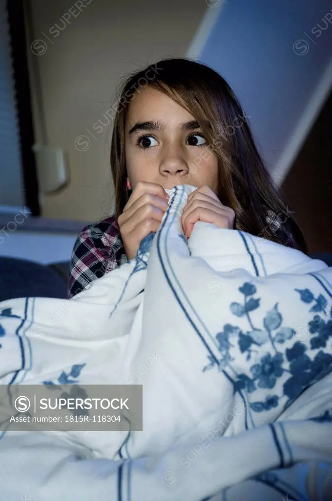 Girl covering her face with bed sheet while watching scary film