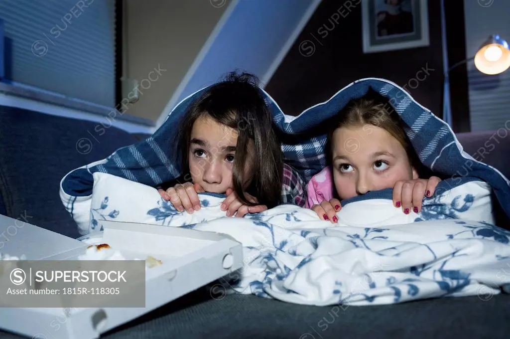 Girls hiding under bed sheet while watching scary film