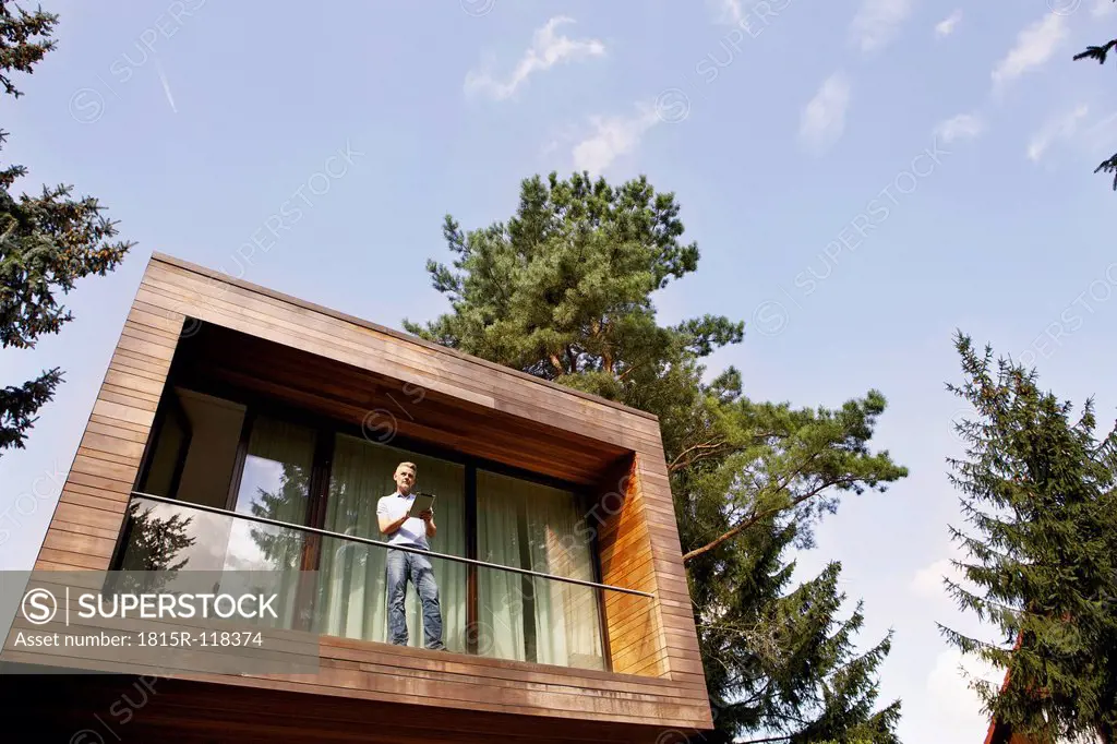 Germany, Berlin, Mature man standing on balcony and using tablet