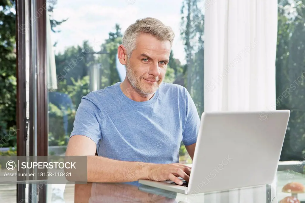 Germany, Berlin, Mature man sitting at table and using laptop