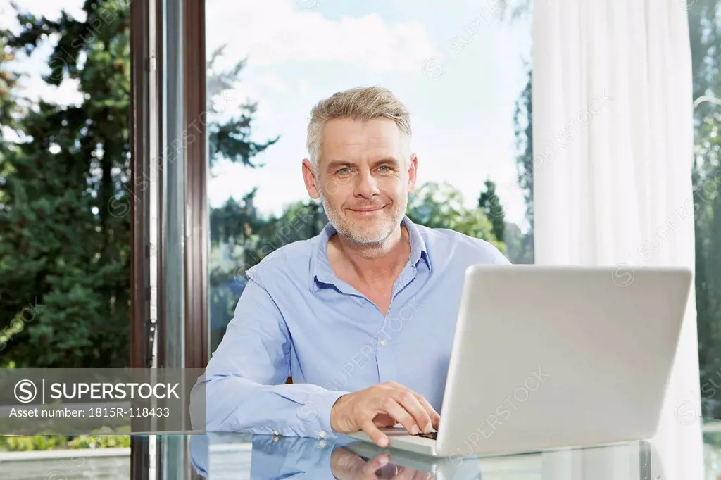 Germany, Berlin, Mature man using laptop, smiling, portrait