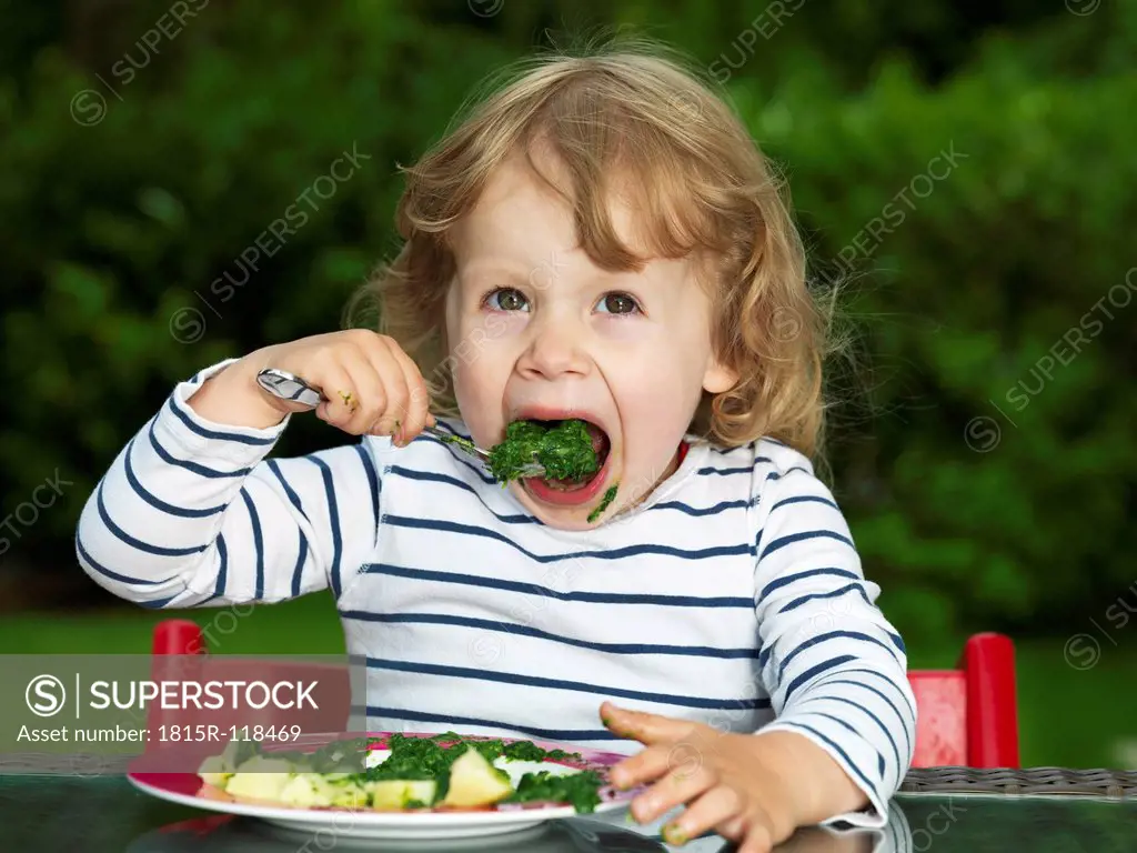 Germany, Duesseldorf, Girl sitting outside and eating spinach, smiling, portrait
