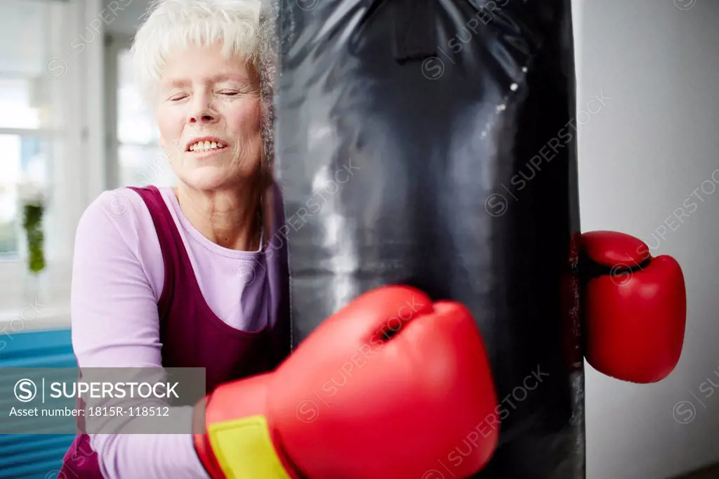 Germany, Duesseldorf, Senior woman with boxing glove and punch bag