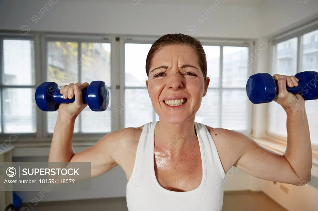 Germany, Duesseldorf, Mature woman exercising with barbell at home